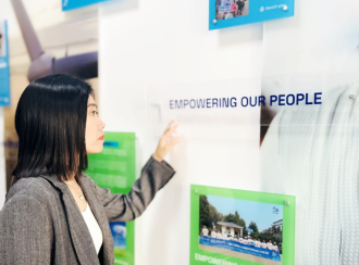 Eine Frau steht vor einem Schild an einer Wand auf dem "Empowering our people" steht.