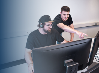 Two service employees in conversation. There are two screens on the desk in front of them.