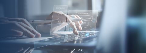 Zwei Hände die auf einer Laptop-Tastatur schreiben, ein Kugelschreiber zwischen den Fingern einer Hand. Ein Kontaktformular wird ausgefüllt.