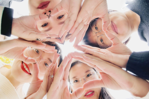 A photo taken from a frog's-eye view with four employees from China forming hearts with their hands and holding them together.