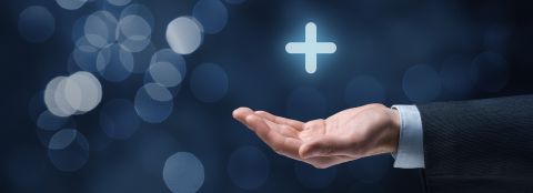A picture with a graphic dark gray-blue background. An outstretched arm holds a plus sign hovering above it as a symbol of added value & service.